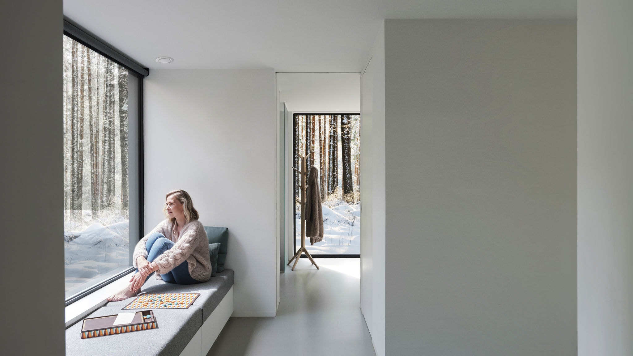 Širok kadar žene koja bosa sjedi ispred prozora i gleda prema van u stabla i snijeg.