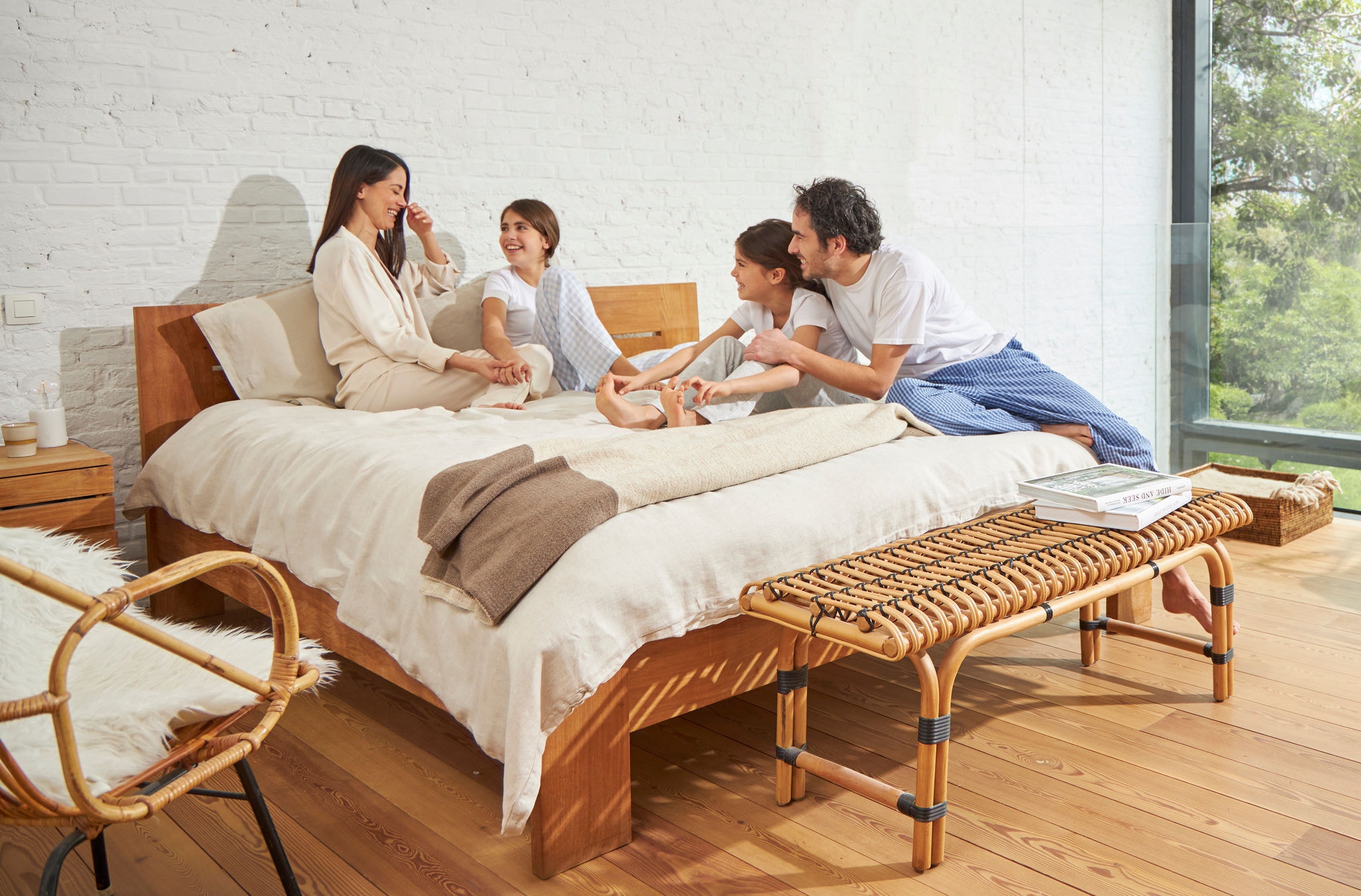 Žena i muškarac koji sjede na krevetu s dvjema djevojčicama, opušteni su, smiju se i uživaju u zdravom zraku.