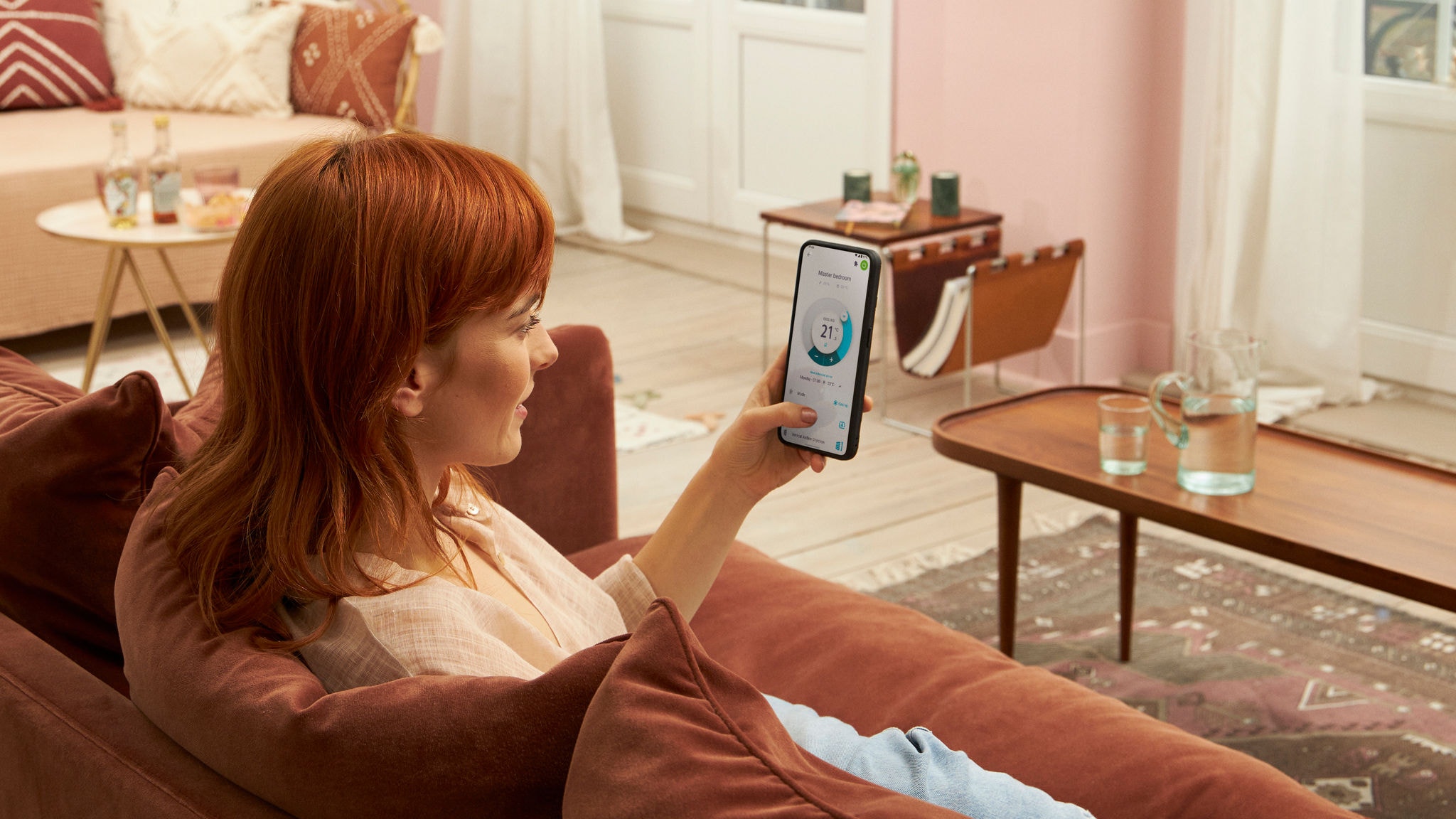 Žena koja sjedi na sofi u svojem domu i upotrebljava aplikaciju Onecta na mobilnom telefonu