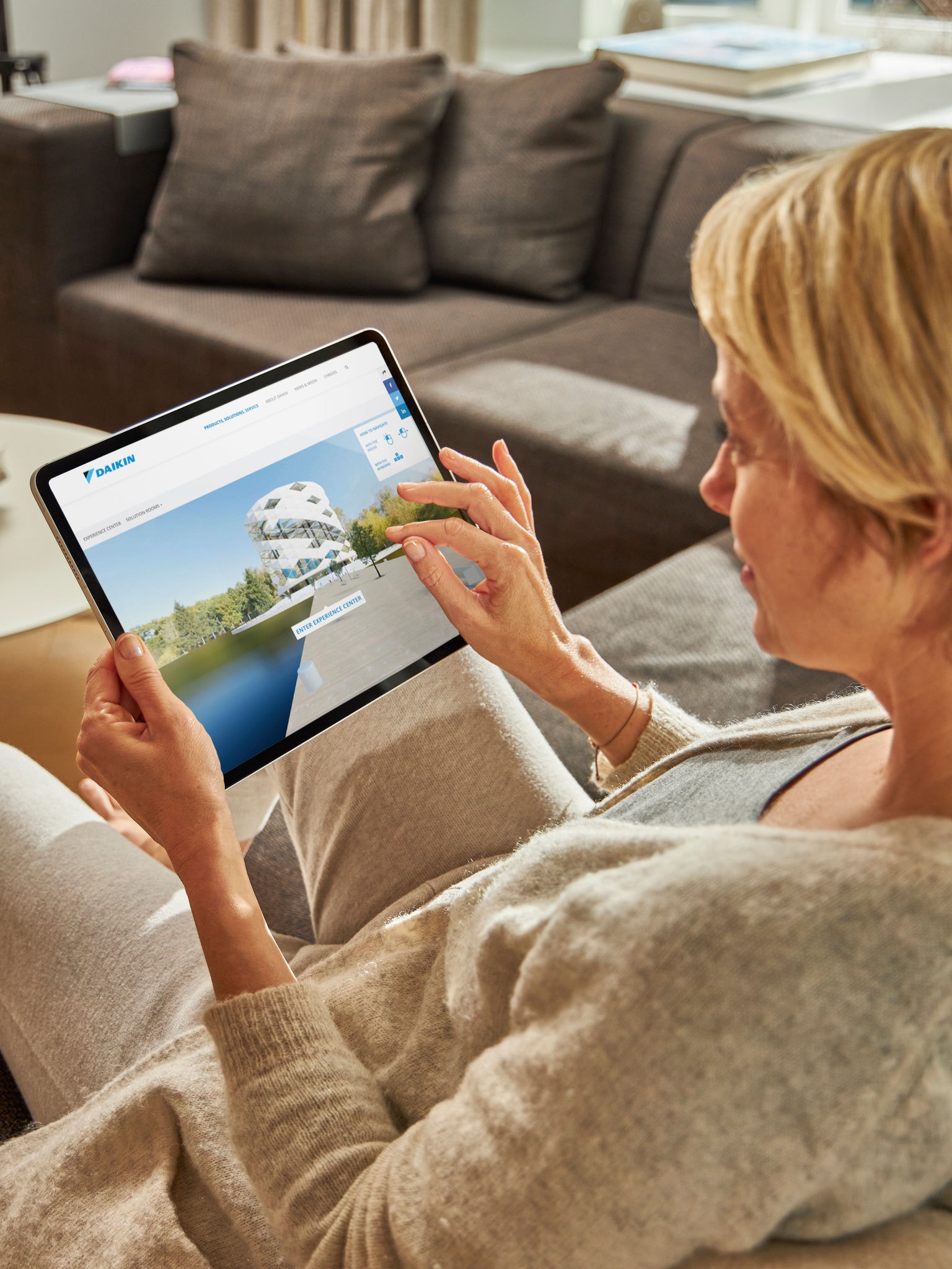 Žena koja posjećuje virtualni experience centar na tabletu dok se opušta na sofi