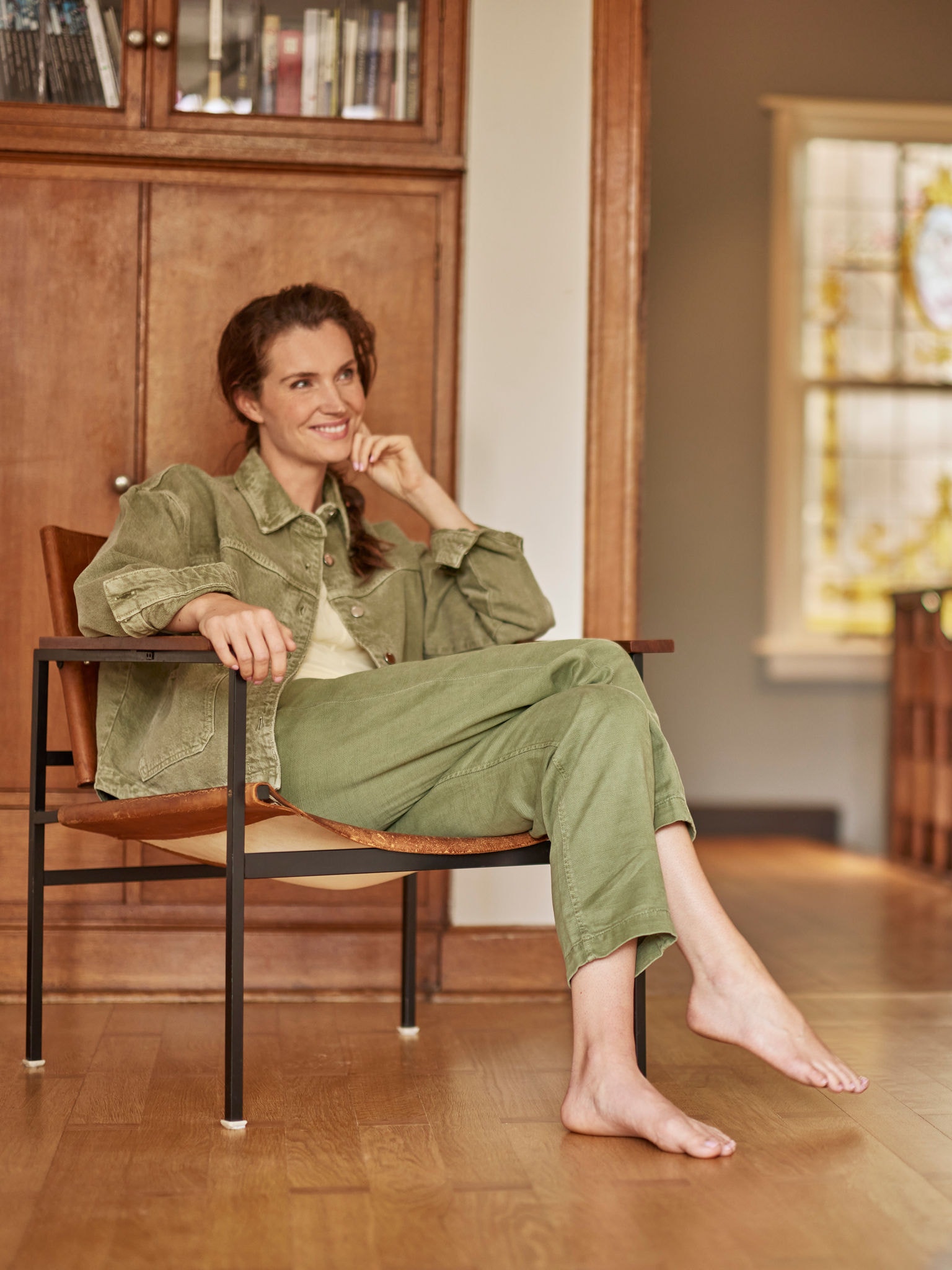 Žena sjedi bosonoga u naslonjaču, smiješi se i gleda prema naprijed