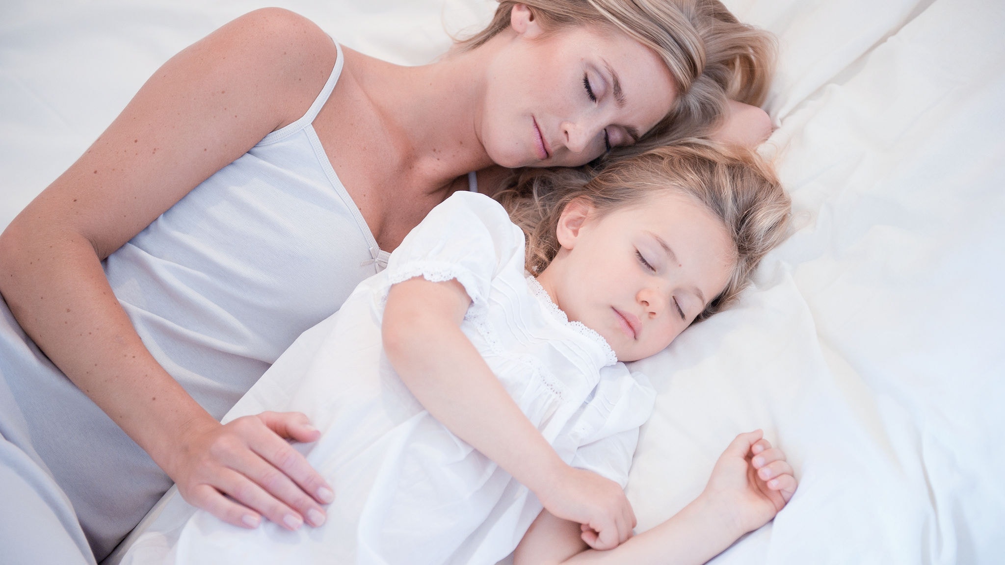 Mama i kćerkica spavaju jedna pored druge u bijelom krevetu na čistom zraku